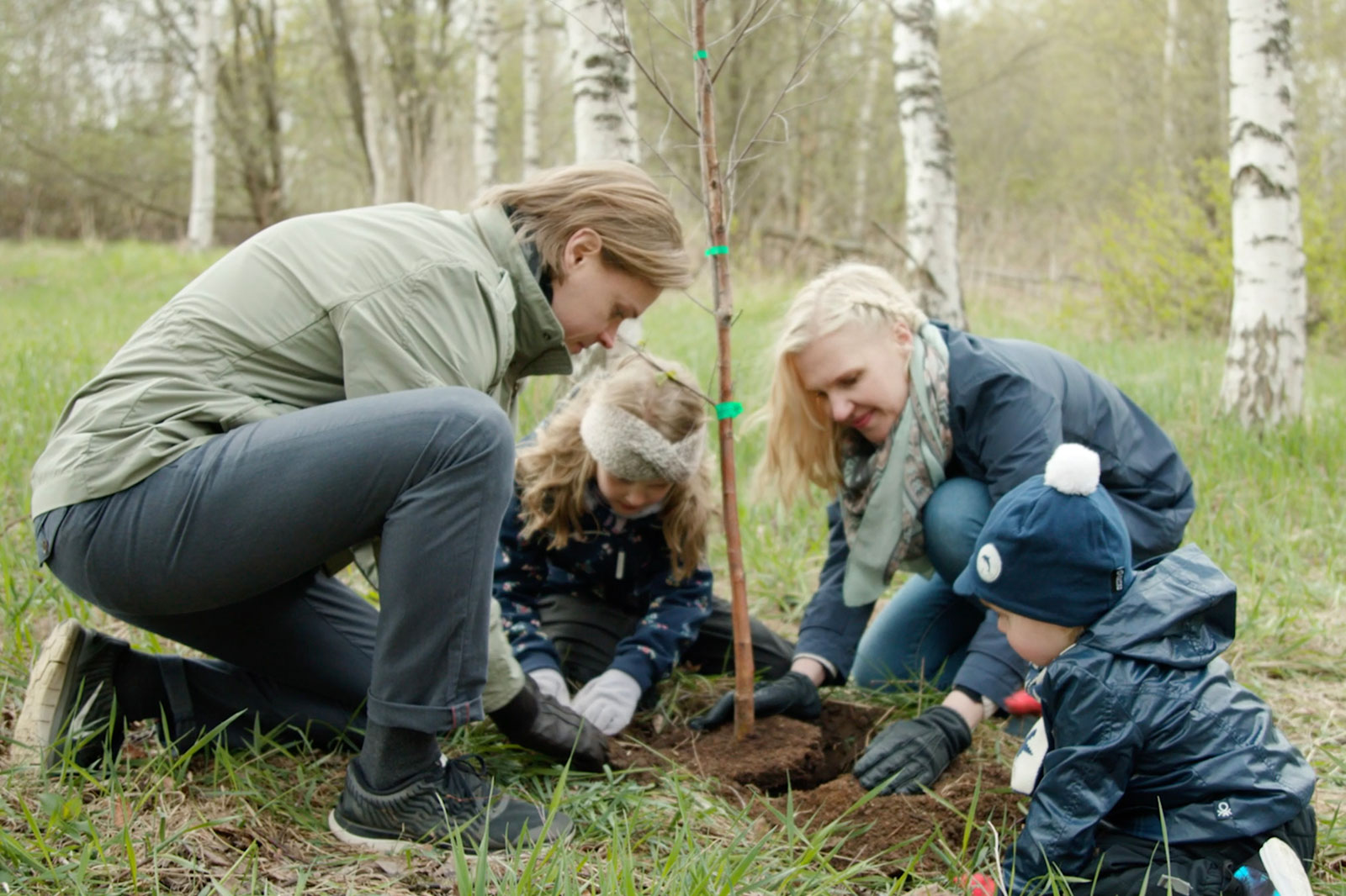 Two adults and two children planting a tree.