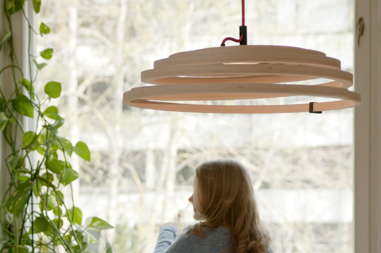 The Aspiro pendant lamp hanging in front of a window. A girl in the background looks out of the window.