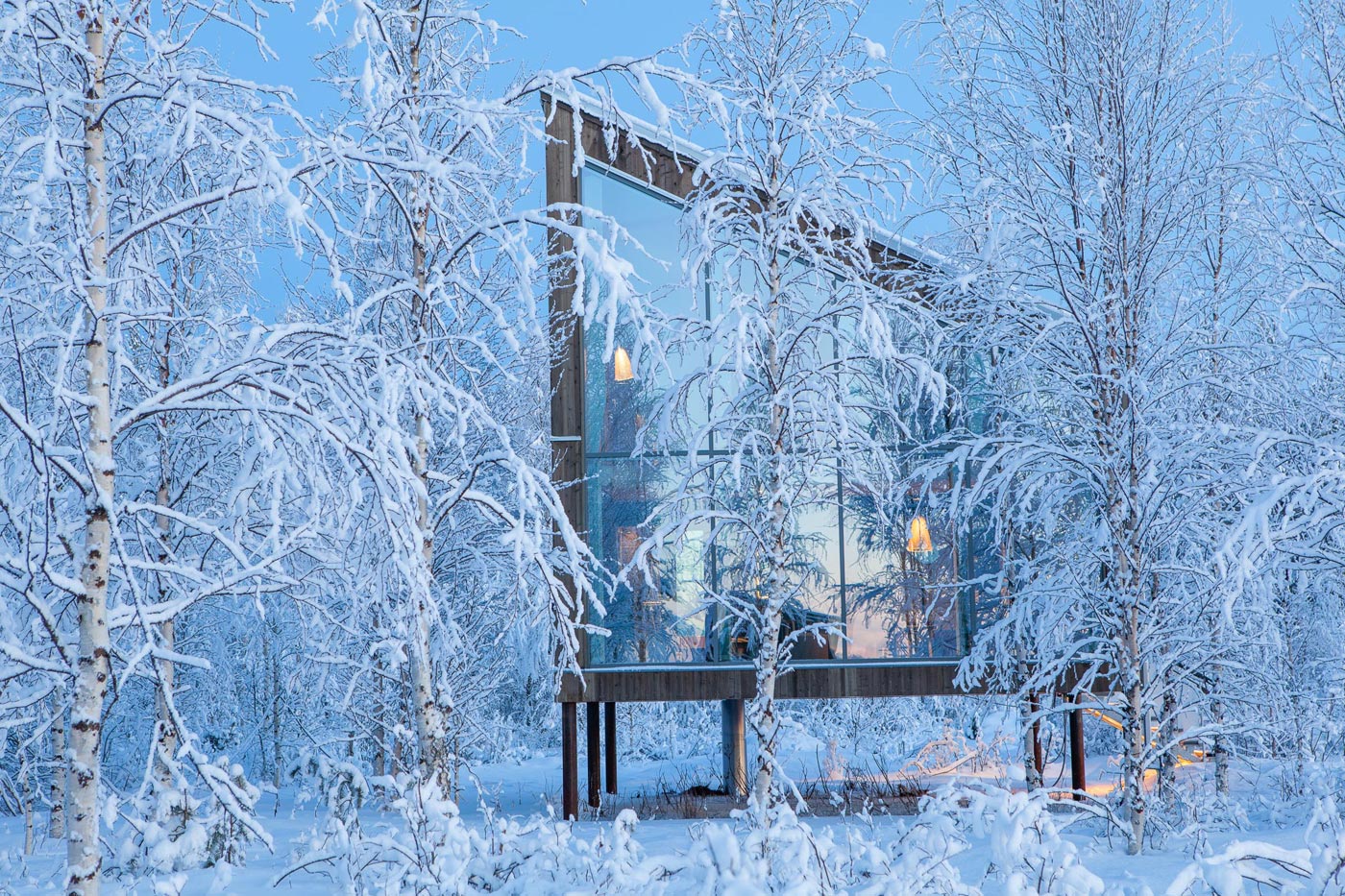 An outside-view of a cabin and frosty landscape. Secto pendant lamps shine through the windows.
