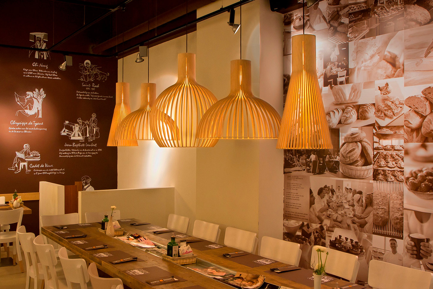 A collection of natural birch Secto Design pendant lamps over a long dining table.