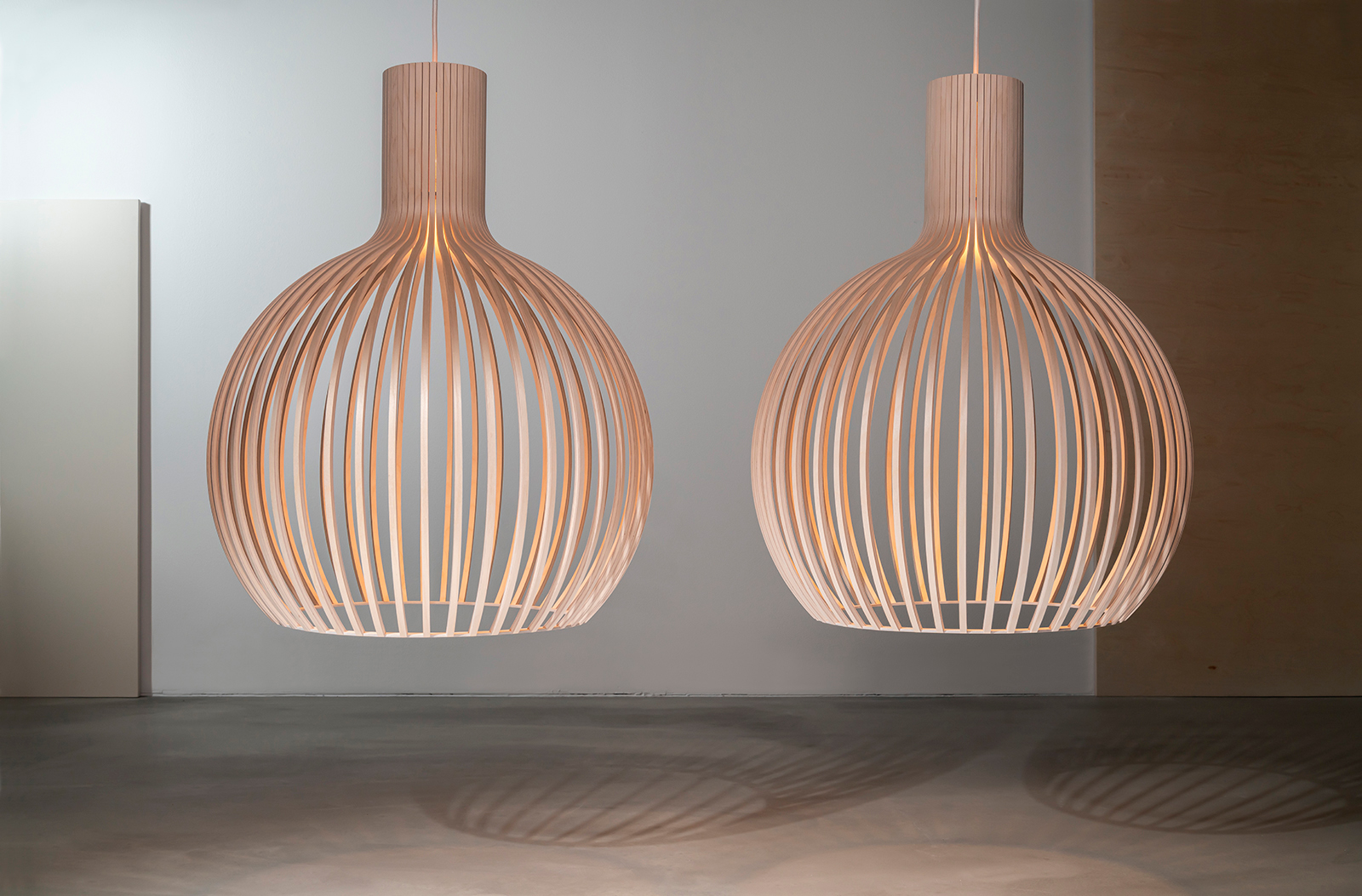 Two Octo pendant lamps in birch hanging side by side in front of a grey background.