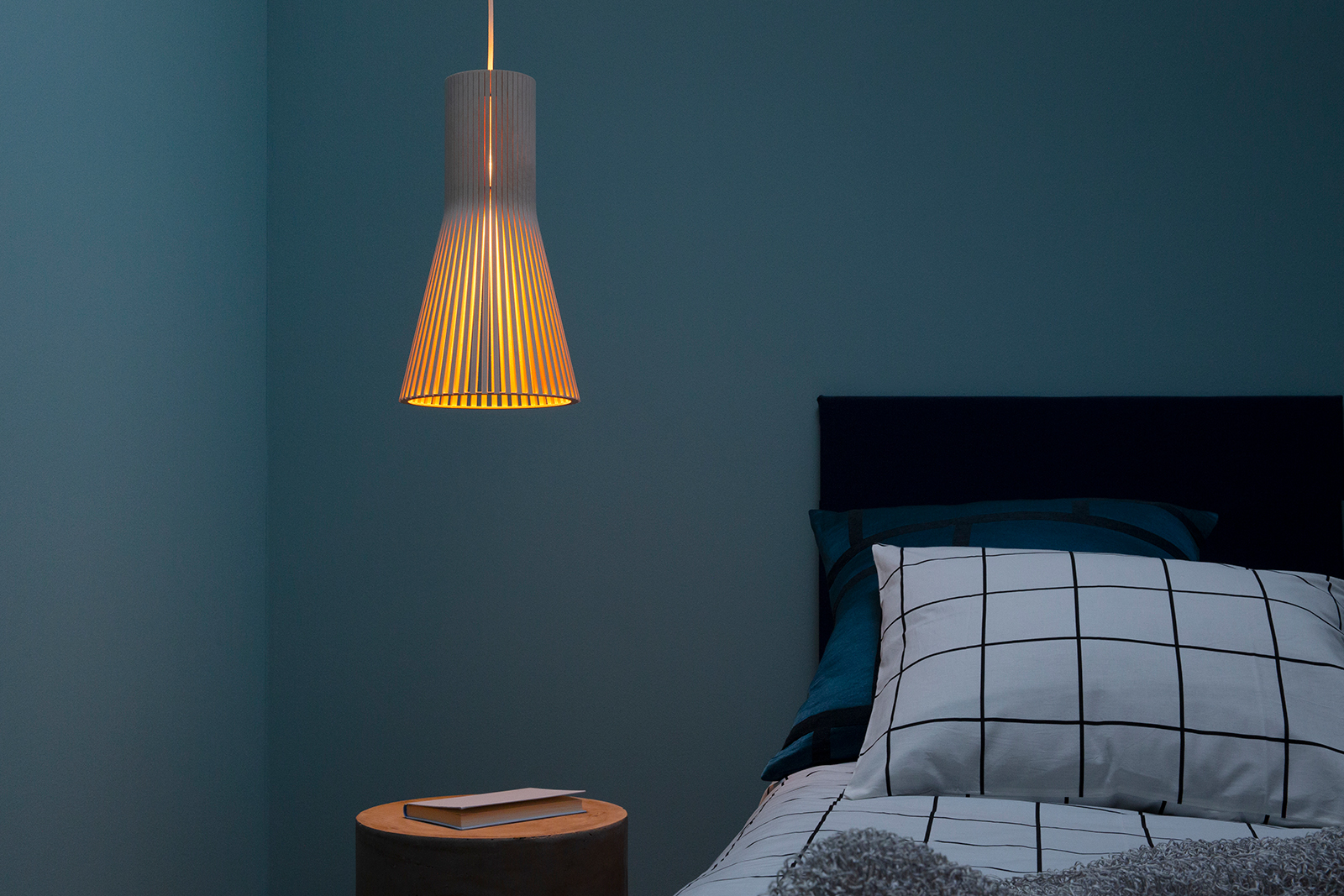 A pendant lamp besides a bed.