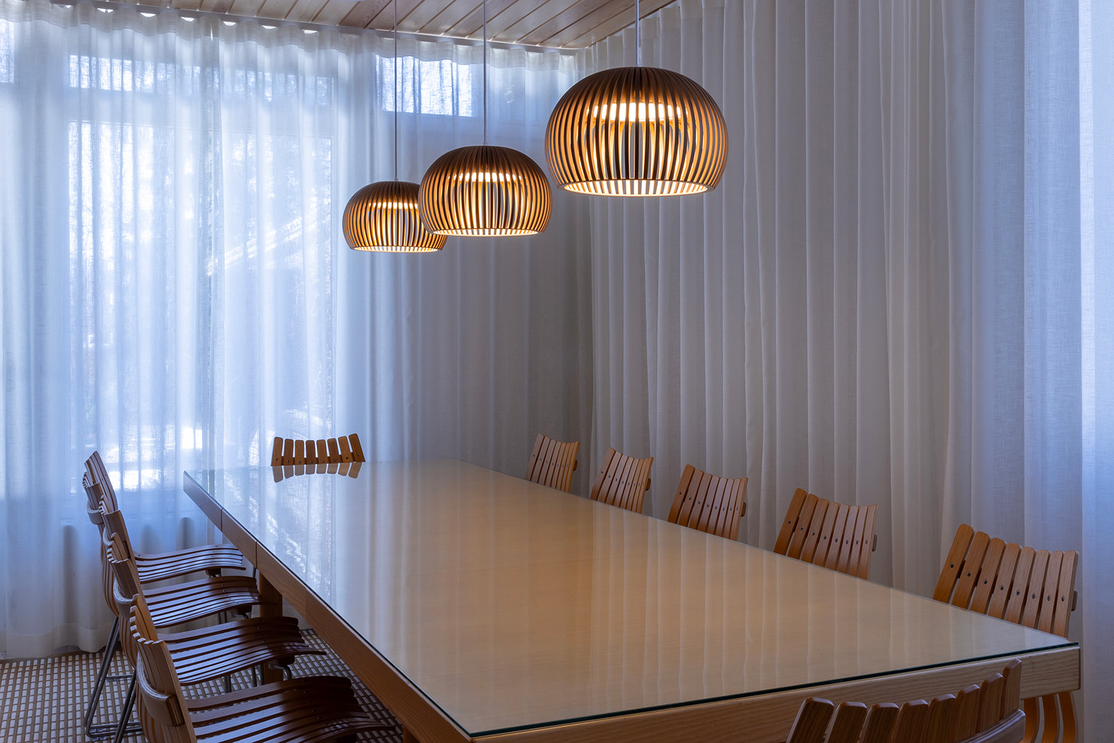 Three pendant lamps above a long conference table. 