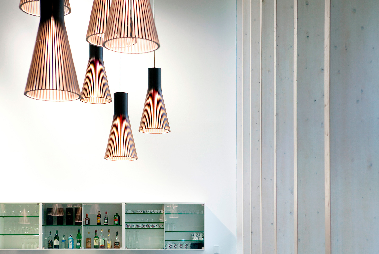 A group of Secto pendant lamps in front of a white wall above a bar.