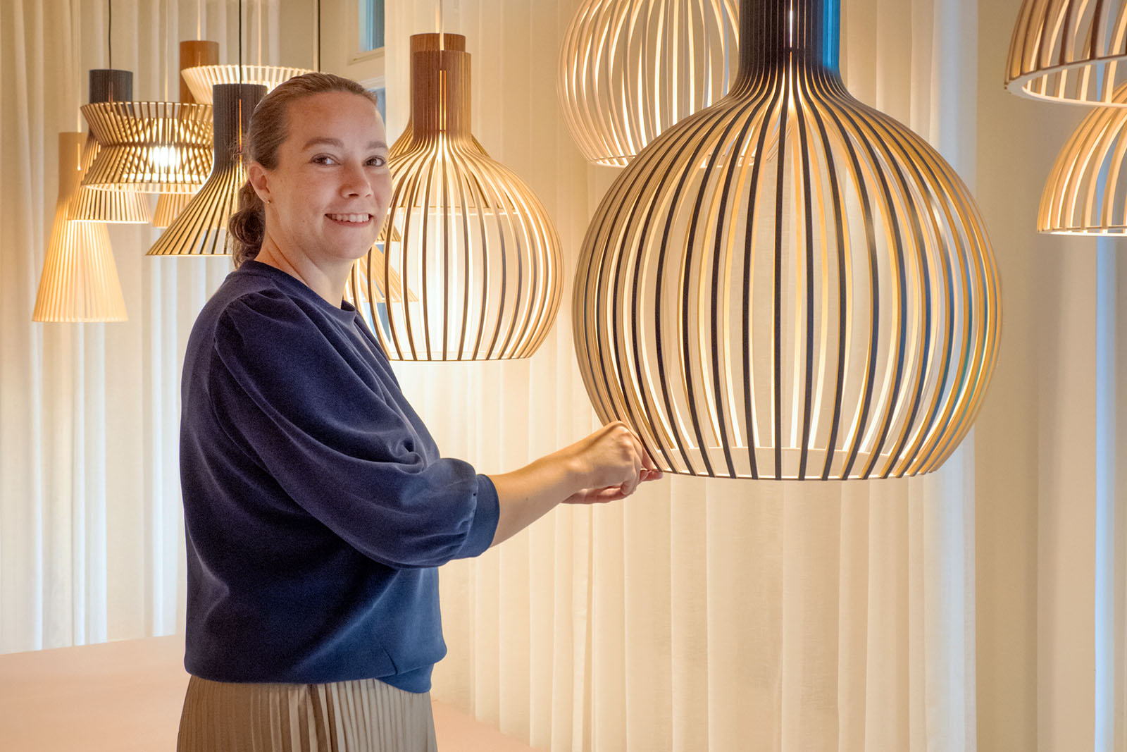 A woman showing a detail of a pendant lamp.