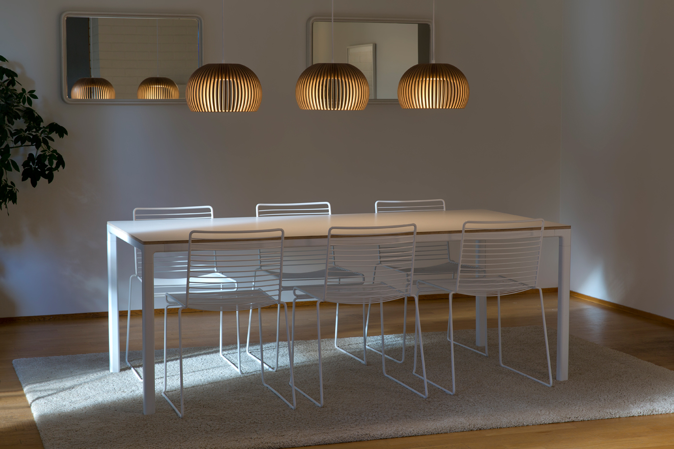 Une table à manger blanche avec six chaises et trois lampes Atto suspendues au-dessus.