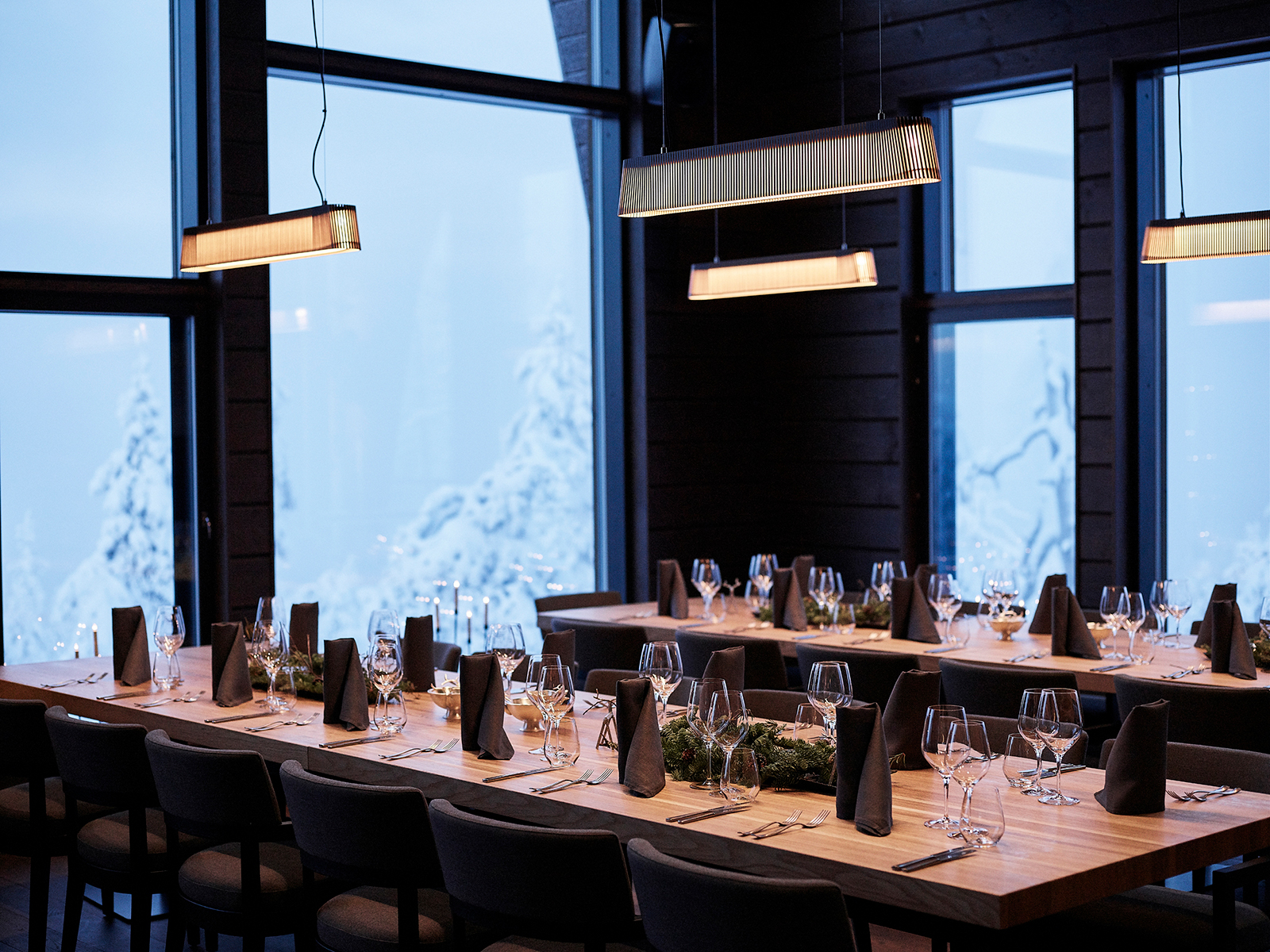 Une salle à manger avec quatre suspensions Owalo et un paysage d'hiver derrière la fenêtre. Les tables sont mises.