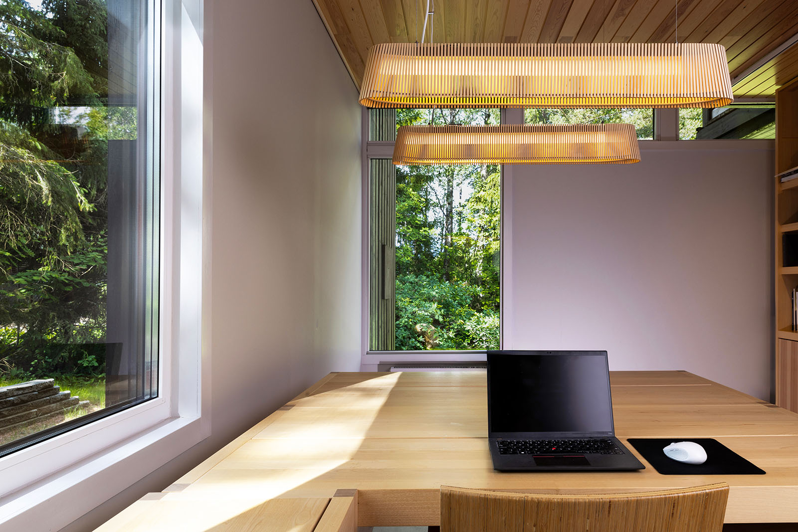 A workstation with two pendant lamps and trees behind the windows.