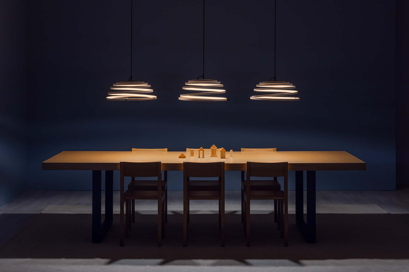 Several enlongated pendant lamps above a meeting table.