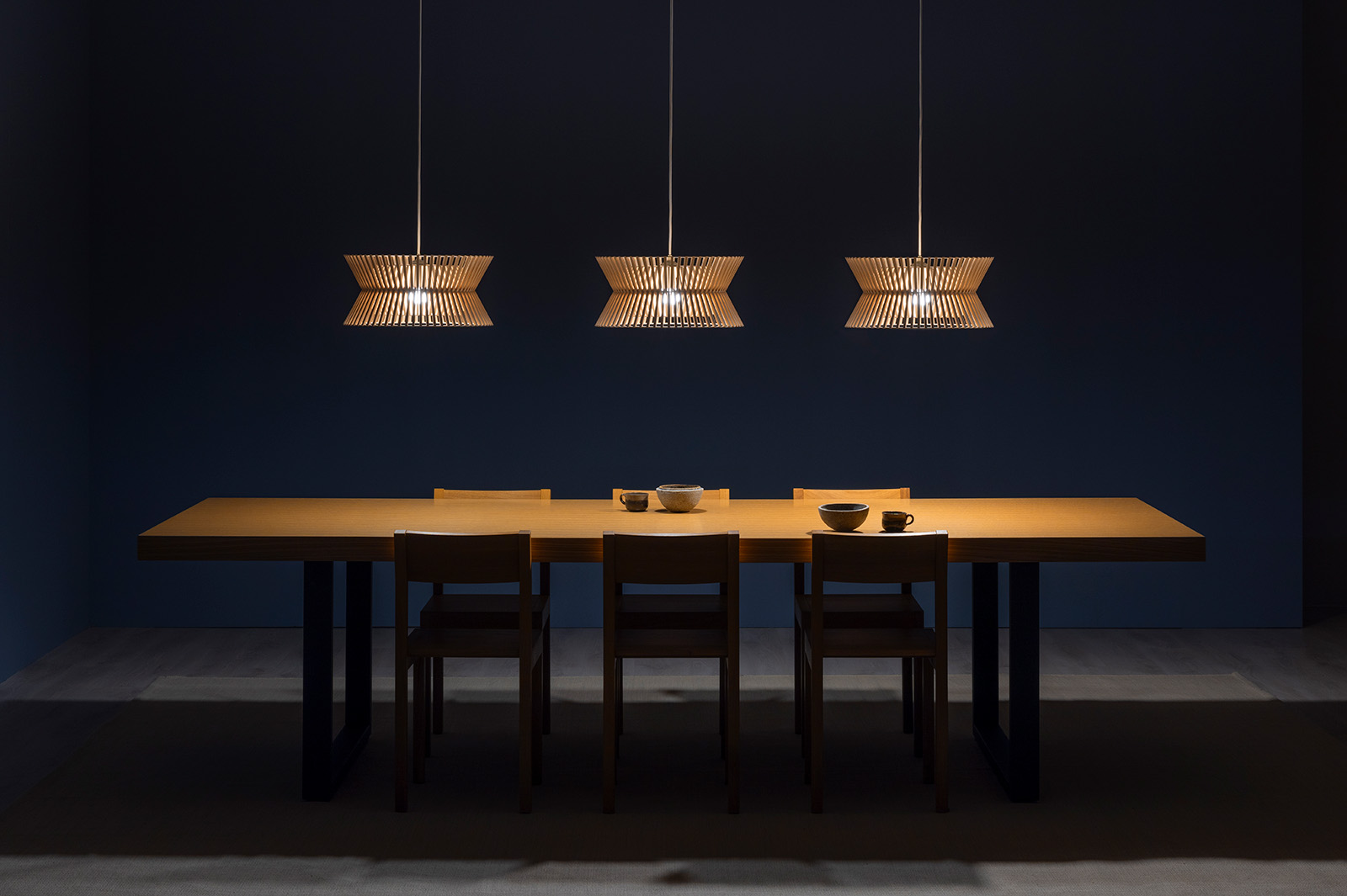 Several enlongated pendant lamps above a meeting table.