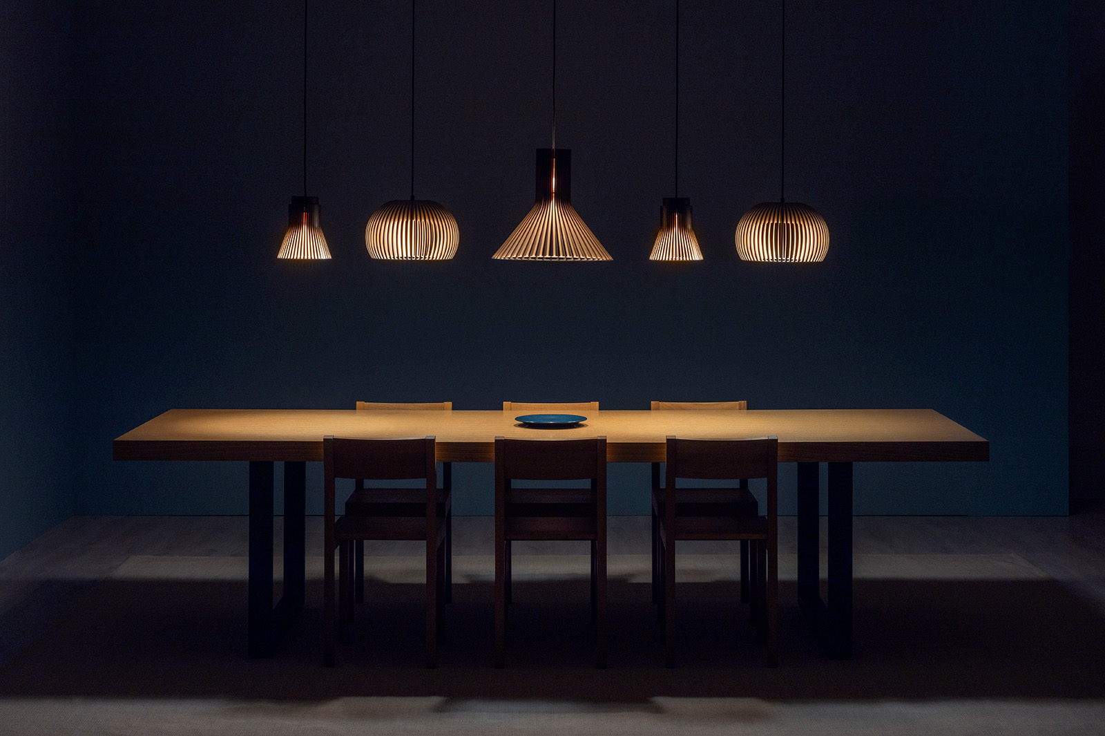 Several enlongated pendant lamps above a meeting table.