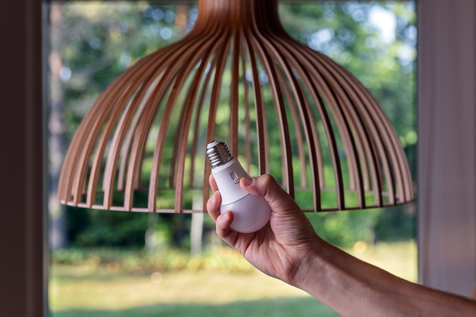 A hand holding a bulb in front of a wooden shade.